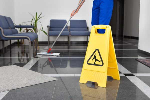 Close-up Of Man Cleaning The Floor With Yellow Wet Floor Sign